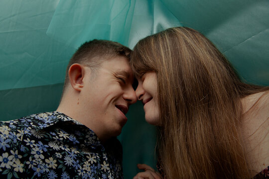 Portrait of young couple with Down Syndrome and Foetal Alcohol Syndrome touching noses in front of blue background