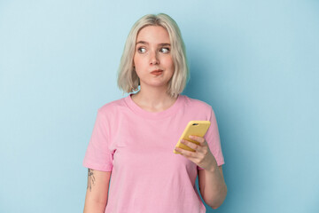 Young caucasian woman holding mobile phone isolated on blue background confused, feels doubtful and unsure.