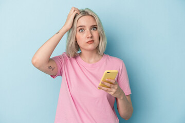 Young caucasian woman holding mobile phone isolated on blue background being shocked, she has remembered important meeting.