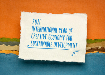 2021 - International Year of Creative Economy for Sustainable Development declared by United Nations, handwriting on a sheet of paper against abstract landscape