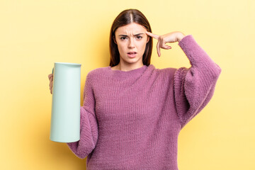 young hispanic woman feeling confused and puzzled, showing you are insane. coffee thermos concept