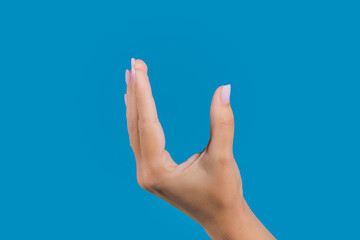 Close-up view photography of beautiful manicured female outstretched up hand making empty cupped gesture isolated on blue background. Fingernails painted with pastel pink gelpolish