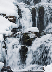 Small waterfall of cold water flow among the stones covered with snow