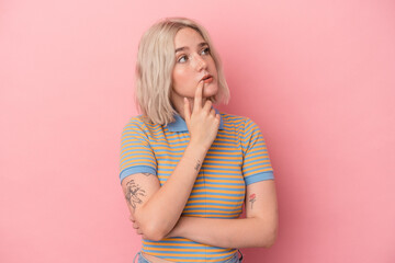 Young caucasian woman isolated on pink background looking sideways with doubtful and skeptical expression.