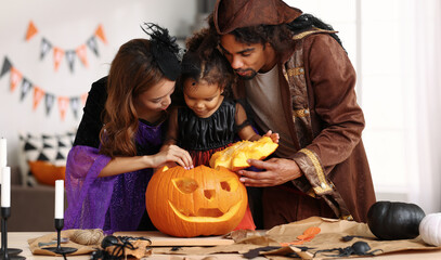 Young african american family in Halloween costumes making together jack o lantern