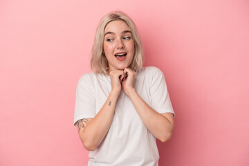 Young caucasian woman isolated on pink background keeps hands under chin, is looking happily aside.