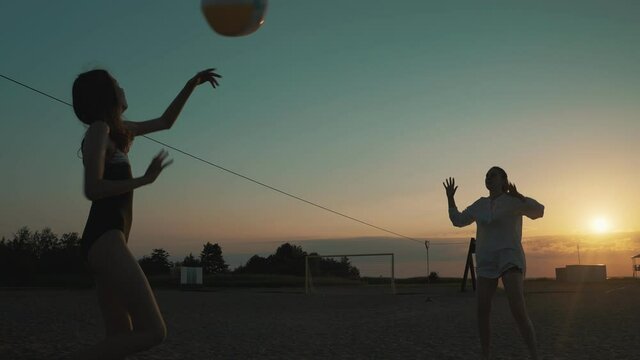Family playing volleyball on the beach at sunset.