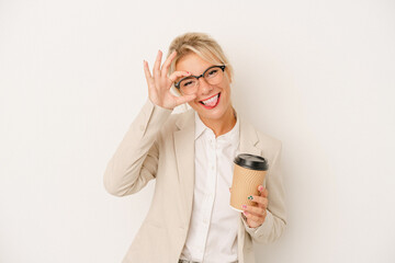 Young business Russian woman holding take away coffee isolated on white background excited keeping ok gesture on eye.