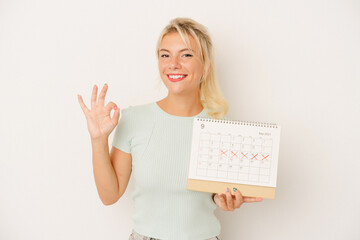Naklejka premium Young Russian woman holding a calendar isolated on white background cheerful and confident showing ok gesture.