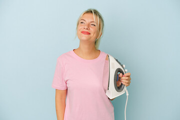 Young Russian woman holding iron isolated on blue background dreaming of achieving goals and purposes