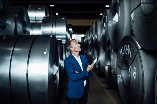 Male inspector with digital tablet checking metals sheet rolls in warehouse