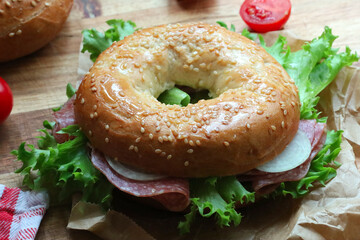 Seeded bagel filled with salad, onions, tomatoes and salami