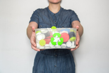 Mujer sosteniendo una caja de reciclaje transparente llena de tapones de botellas. Reciclar logo en...