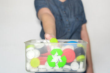 Mujer sosteniendo una caja de reciclaje transparente llena de tapones de botellas. Reciclar logo en...