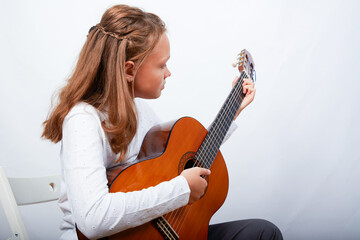 Fototapeta premium an 11-year-old girl is practicing a melody on a guitar on a blue background