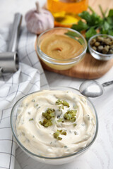Tasty tartar sauce and ingredients on white table