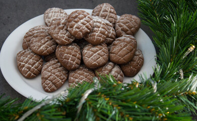 Chocolate cookies on a white plate. Christmas biscuits close up photo. Fir tree branches, anise stars, cinnamon sticks pine cone shaped cookies. Sweet food top view photo. 