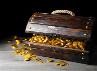 Open treasure chest with gold coins on grey wooden table