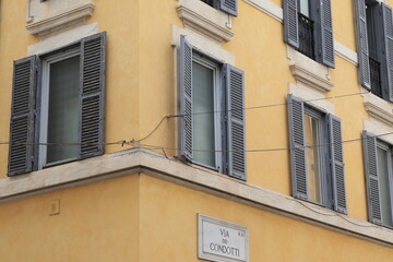 Fototapeta na wymiar Yellow Ochre Building Facade Detail with Windows and Open Shutters in Rome, Italy