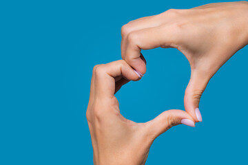 Horizontal color photography of white young adult woman making heart gesture with 2 hands isolated on bright blue background