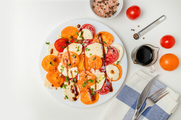 Fresh classic italian caprese salad with sliced red yellow tomatoes, mozzarella, olive oil, pepper and salt on light background. Healthy vegetarian diet food