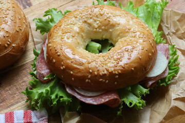 Seeded bagel filled with salad, onions, tomatoes and salami