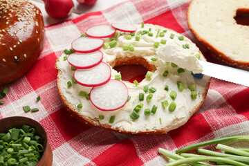 Delicious bagel with cream cheese, green onion and radish on table, closeup