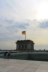 View of Reichstag rooftop with German national flag and people walking during in summer. Clouds in blue and yellow sunset sky background.