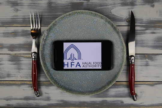 Viersen, Germany - June 9. 2021: Closeup of smartphone with logo lettering of hfa halal food authority on plate with cutlery (focus on center)