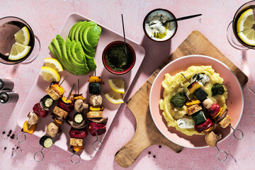 Roasted Veggie Kebabs with tofu and mushrooms , avocado and basil pesto. tzatziki sauce and summer cocktail on a pink table . and mashed potatoes