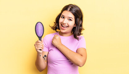 young hispanic woman feeling happy and facing a challenge or celebrating. hairbrush concept