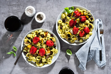 orecchiette pasta with pesto and baked cherry tomatoes on the stone background with red wine in the glasses