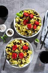 orecchiette pasta with pesto and baked cherry tomatoes on the stone background with red wine in the glasses