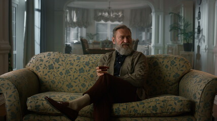 Fototapeta premium Thoughtful mature man thinking with alcohol glass. Rich old grandfather relaxing