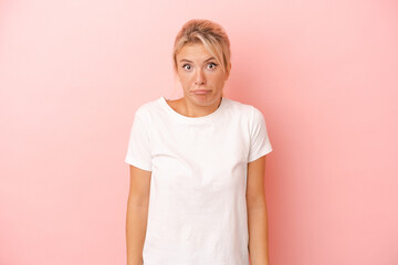 Young Russian woman isolated on pink background shrugs shoulders and open eyes confused.