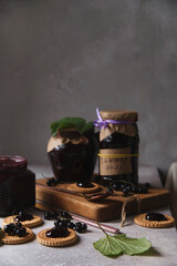 Black currant jam in glass jars with black currant berries and green leaves on white table.