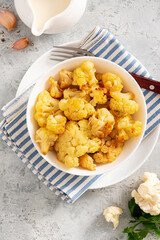 Baked cauliflower in a white bowl on a gray background. Homemade baked cauliflower with butter, cream and garlic. Tasty vegetarian food.