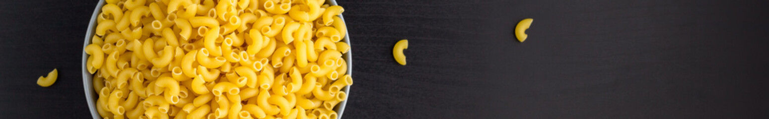 banner of Top view of black background with italian raw pasta horns in bowl with copy space