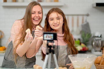 Caucasian family with mother and daughter show cookies or cake to camera during live streaming or online present to other people for new modern lifestyle in their home kitchen.