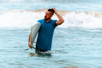 Surfer z deską na wybrzeżu przygotowujący się do pływania. - obrazy, fototapety, plakaty