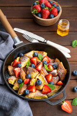 Kaiserschmarrn - traditional austrian pancake dessert with fresh berries and powdered sugar on a dark wooden background. Sweet breakfast. Copy space.