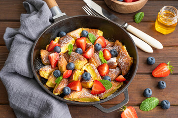 Kaiserschmarrn - traditional austrian pancake dessert with fresh berries and powdered sugar on a dark wooden background. Sweet breakfast. Copy space.