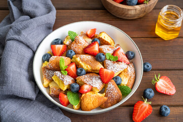 Kaiserschmarrn - traditional austrian pancake dessert with fresh berries and powdered sugar on a dark wooden background. Sweet breakfast. Copy space.