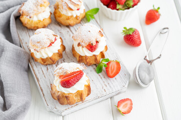 Delicious homemade small cakes profiterole choux pastry with custard, strawberry and icing powder on the white wooden background. Copy space.