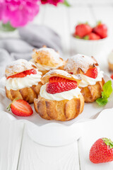 Obraz na płótnie Canvas Delicious homemade small cakes profiterole choux pastry with custard, strawberry and icing powder on the white wooden background. Copy space.