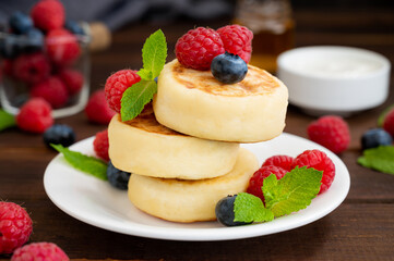 Cottage cheese pancakes with fresh berries, sour cream and honey on a dark wooden background. Homemade traditional Ukrainian and Russian syrniki.