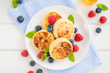 Cottage cheese pancakes with fresh berries, sour cream and honey on a white wooden background. Homemade traditional Ukrainian and Russian syrniki.