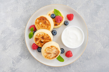 Cottage cheese pancakes with fresh berries, sour cream and honey on a gray concrete background. Homemade traditional Ukrainian and Russian syrniki.