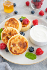 Cottage cheese pancakes with fresh berries, sour cream and honey on a gray concrete background. Homemade traditional Ukrainian and Russian syrniki.