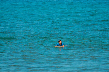 Surfer mężczyzna łapiący falę na desce na tle niebieskiego oceanu i błękitnego nieba. - obrazy, fototapety, plakaty